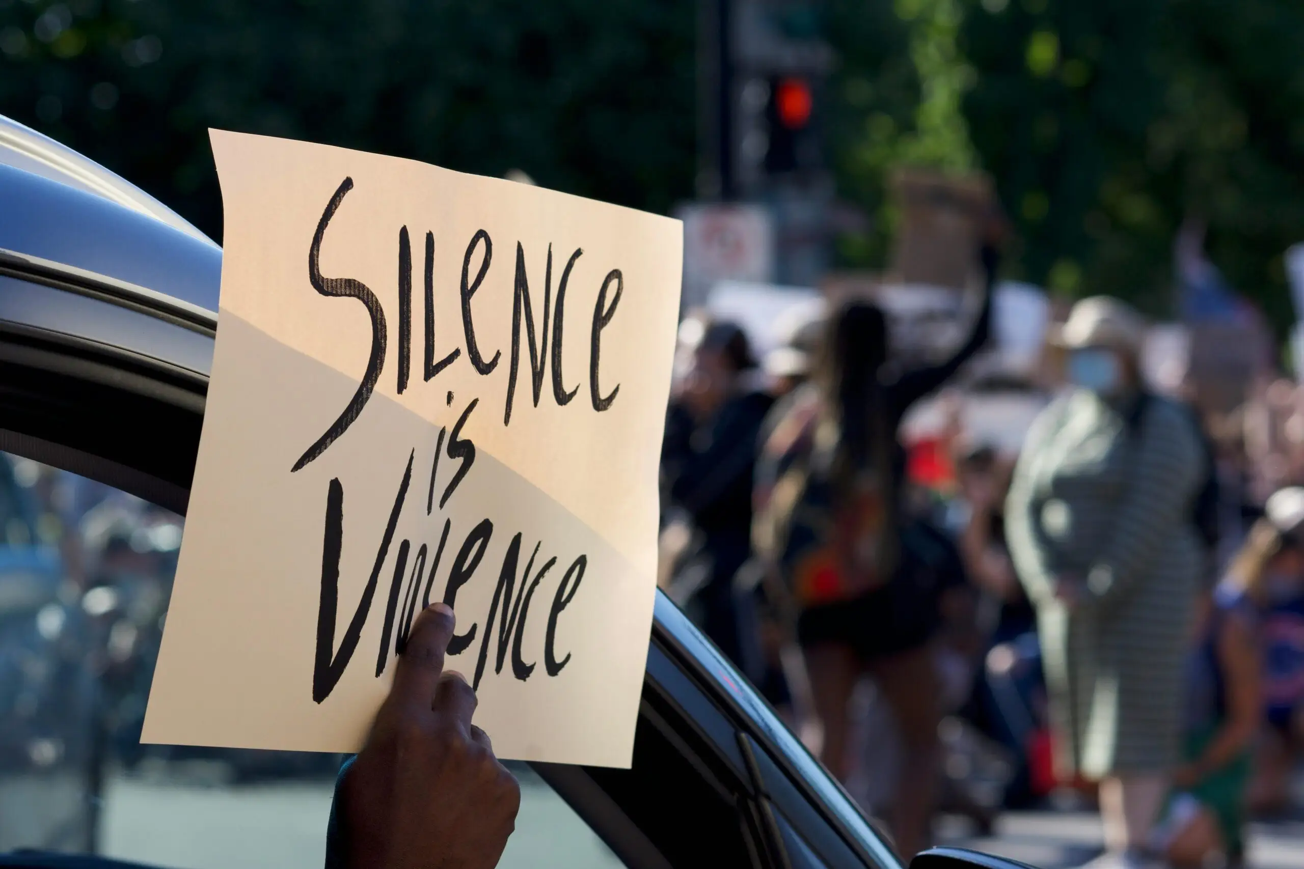 Protest sign saying 'Silence is Violence' held at a peaceful outdoor protest.