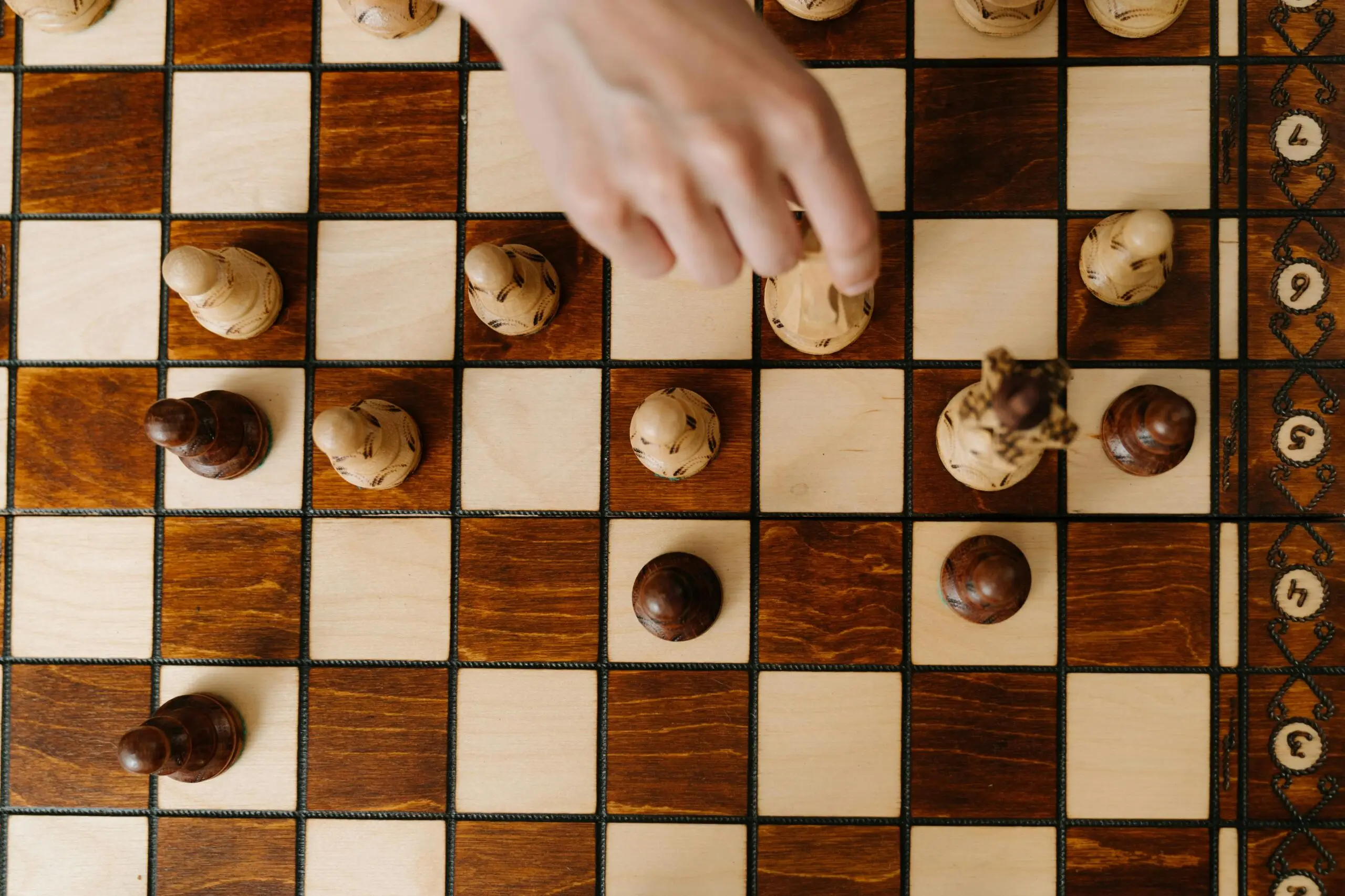 A hand moving a chess piece during gameplay, emphasizing strategy and tactics from a top-down perspective.