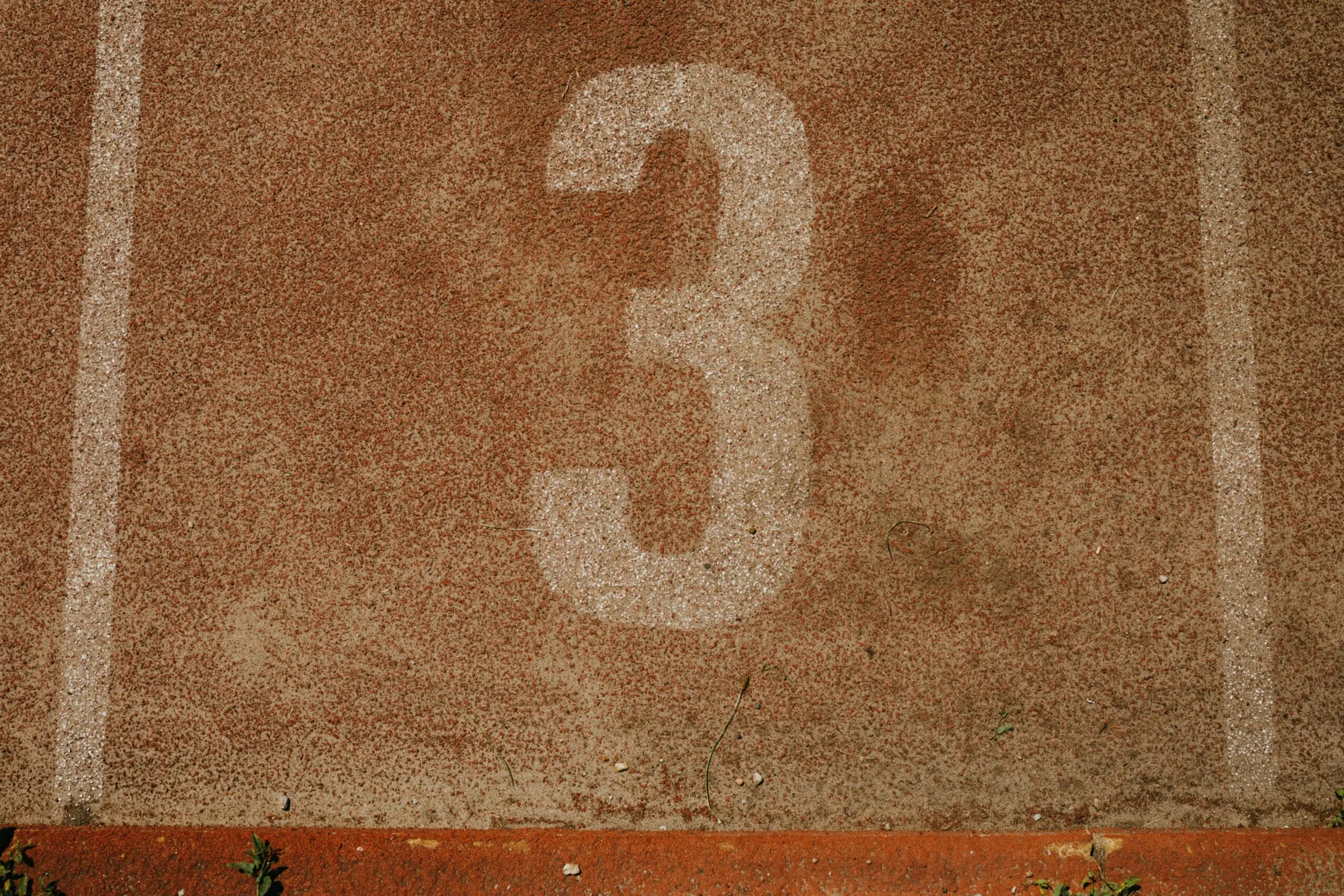 Close-up of a textured running track with the number three, showcasing sport simplicity and earthy tones.